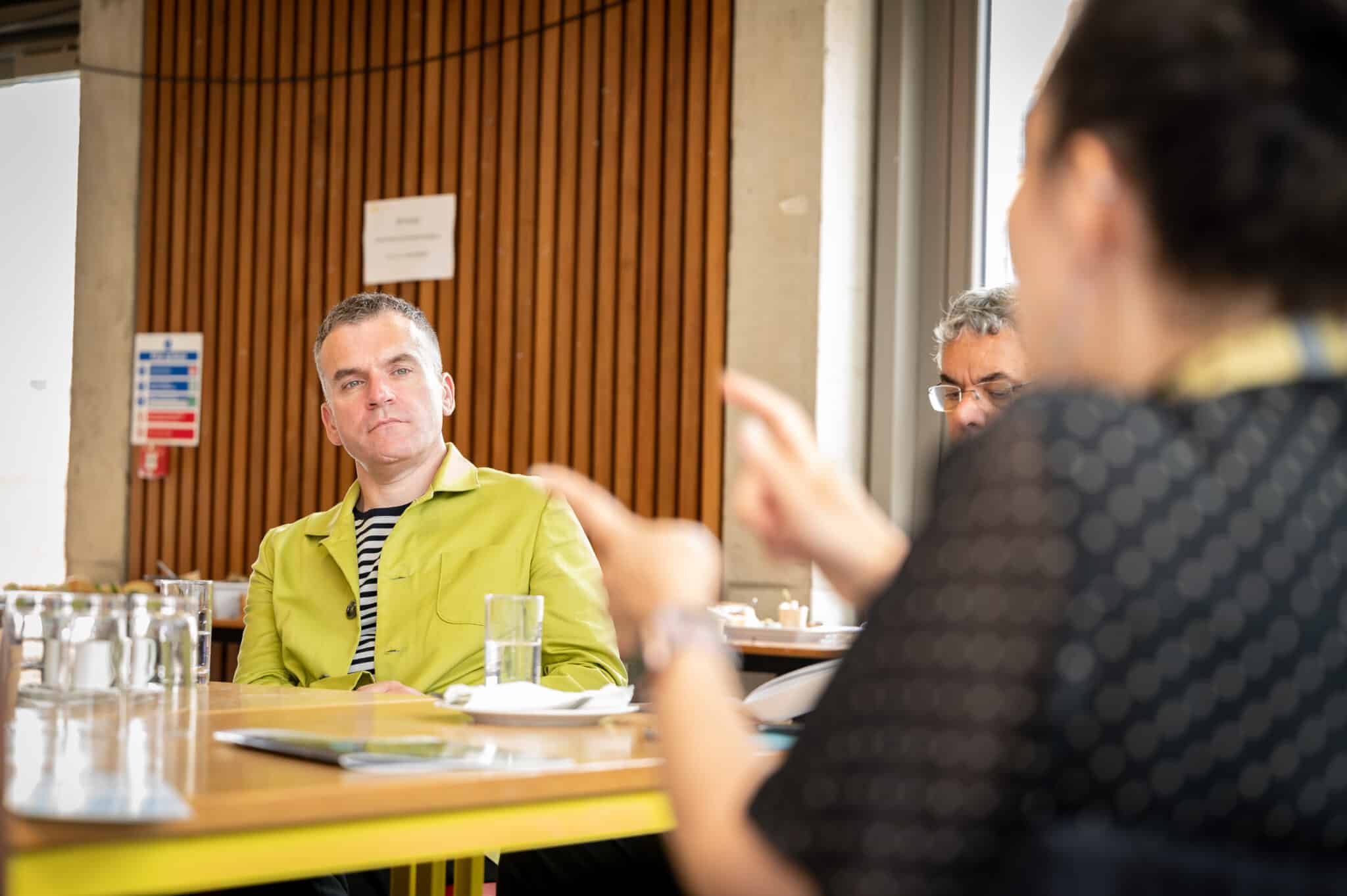 White man sitting attentively at a table in a yellow jacket