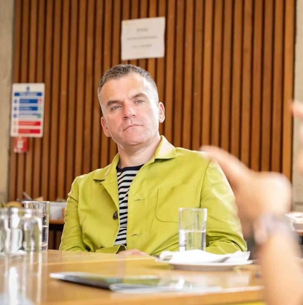 White man sitting attentively at a table in a yellow jacket