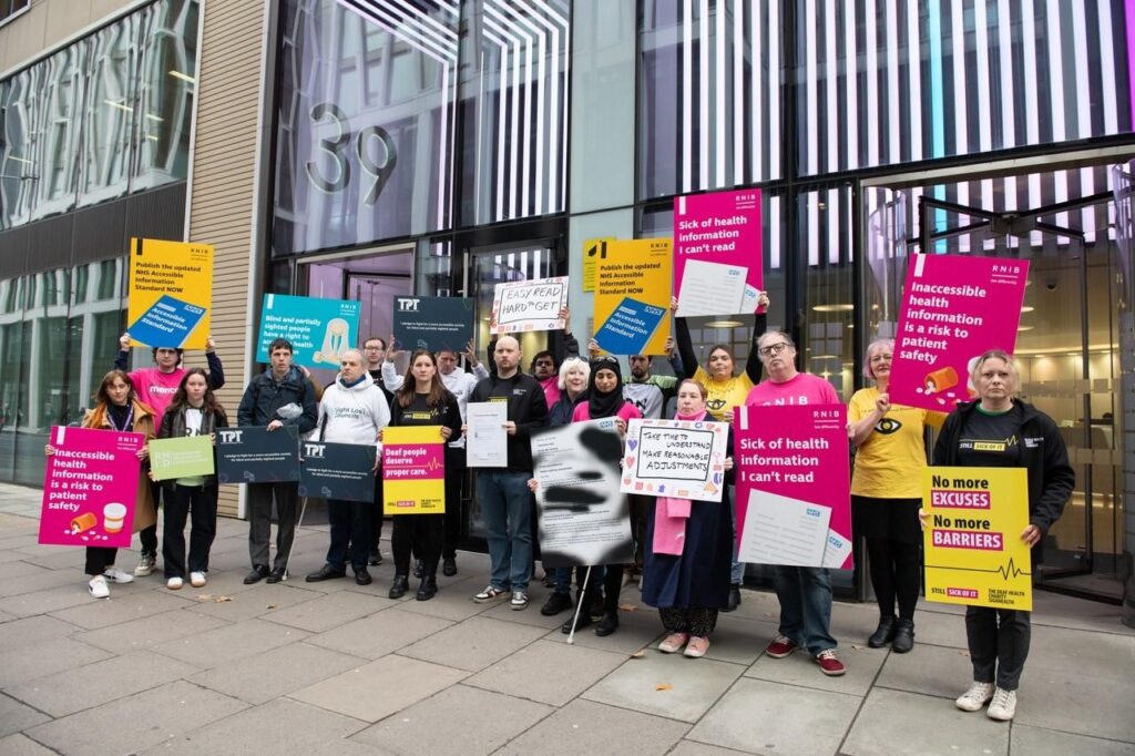 Group of people standing together holding placards in front of Department of Health