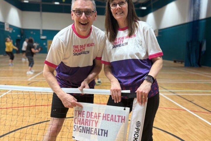 Pickleball court indoors, two people wearing SignHealth t shirts holding SignHealth branded logo banner