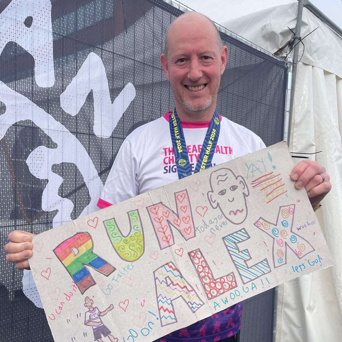 Male runner for signhealth in charity t shirt holding banner saying run Alex