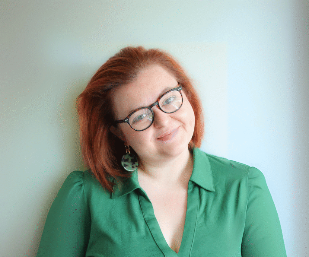 Woman with glasses, red hair and green shirt smiling