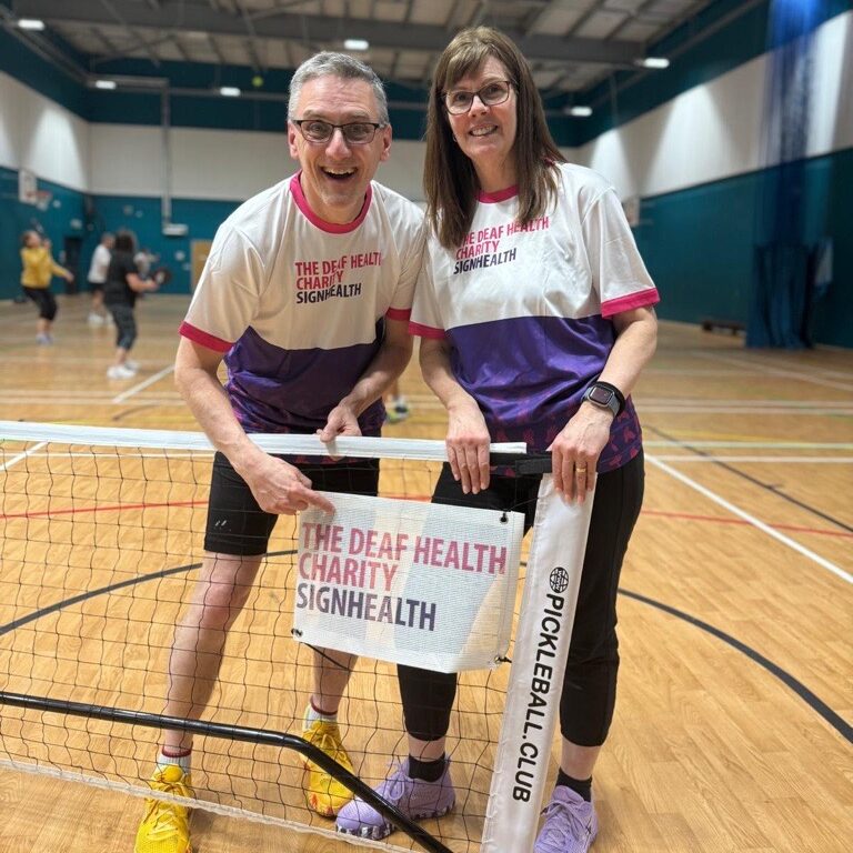 Pickleball court indoors, two people wearing SignHealth t shirts holding SignHealth branded logo banner