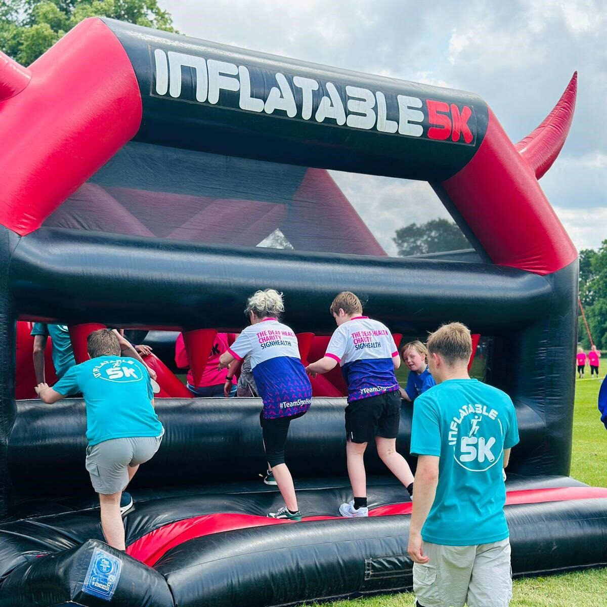 Two people fundraising for SignHealth in branded t shirts climbing up inflatable course
