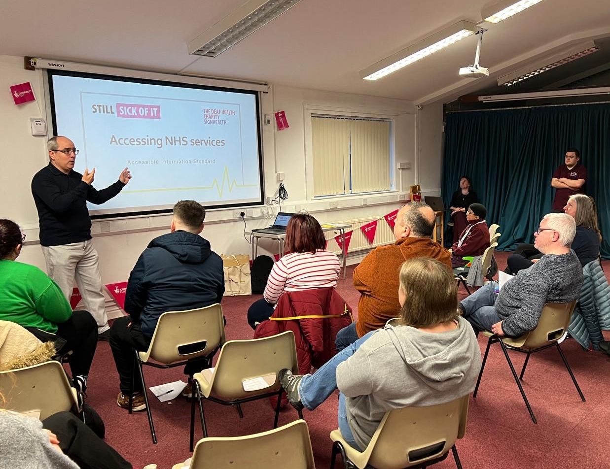 Workshop a group of people sat listening and watching a workshop delivered by SignHealth