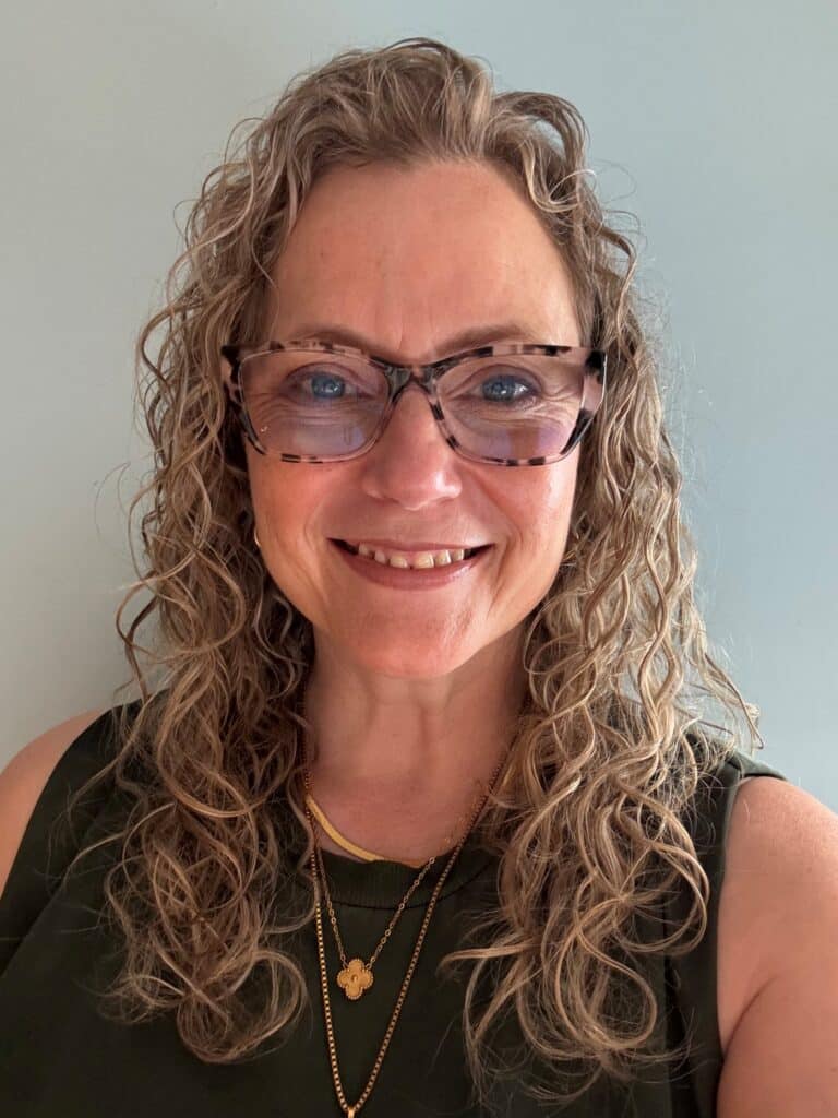 Curly hair woman with tinted glasses, wearing green top 